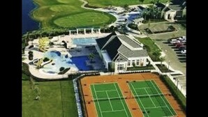 Vista aérea de un complejo turístico con una gran piscina, canchas de tenis y un campo de golf.