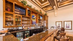 Zona de bar con encimera de granito, estantes de madera con botellas, vasos y una pantalla de televisión.