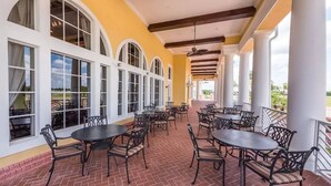 Un patio exterior techado con suelo de ladrillo, columnas blancas y varias mesas y sillas.