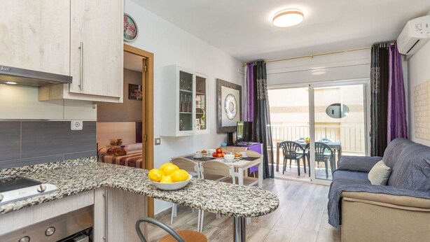 Una cocina compacta con encimera de granito, un comedor con mesa y sillas, y una sala de estar con sofá.