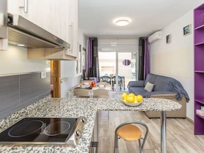 A compact kitchen with a built-in stove, a dining area with a table and chairs, and a living area with a sofa and a purple bookshelf.