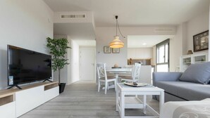 A modern living room with a flat-screen TV, a dining area with white furniture, and a grey sofa. - Beautiful apartment for 4 guests with WIFI, pool, A/C, TV and terrace (Cambrils)
