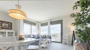 A modern living room with a sofa, chairs, a dining table, and a large window. - Beautiful apartment for 4 guests with WIFI, pool, A/C, TV and terrace (Cambrils)