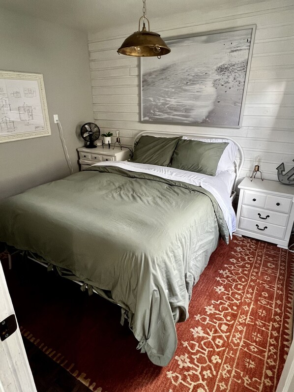 Un dormitorio con una cama, una mesita de noche, una lámpara, un reloj de pared y una alfombra estampada.