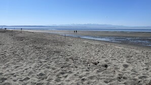 Une plage avec un ciel dégagé, des montagnes lointaines et quelques personnes qui se promènent.