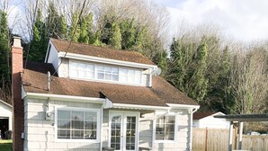 Une maison à deux étages avec un porche, une cour clôturée et une pancarte indiquant « Maison de plage ».