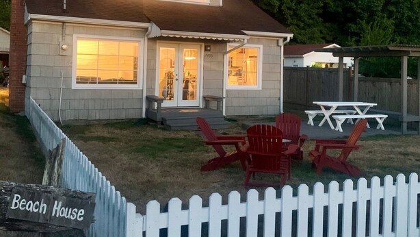 Une maison à deux étages avec un patio couvert, une cour clôturée et une pancarte indiquant « Maison de plage ».