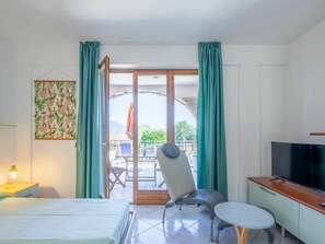 Ein Hotelzimmer mit einem Bett, einem Schreibtisch, einem Fernseher, einem Sessel und einem Balkon mit Tisch und Stühlen.