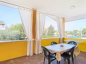 Ein Balkon mit gelben Wänden, einem Tisch, zwei Stühlen und weißen Vorhängen.