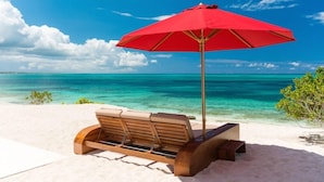 A wooden bench with a red umbrella on a sandy beach with clear turquoise water and a blue sky. - Beach Kandi 15% off stays in Fall 2026 | Beach Front - Located in  Magnificent Grace Bay with House Cleaning Included (Providenciales)