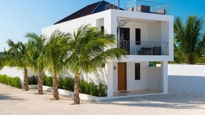 Un bâtiment moderne à deux étages, doté d’un balcon, entouré de palmiers et bordé d’une allée en gravier.