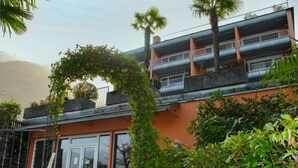 Ein modernes Gebäude mit Glastür, einem Balkon mit Metallgeländern und üppiger Bepflanzung rundherum.