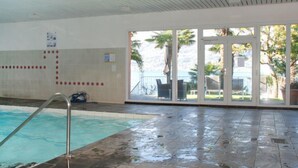 Ein überdachter Pool mit Glastür zu einem Außenbereich mit Palmen.
