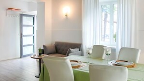 Ein Essbereich mit Tisch für zwei Personen, einer Couch und einem Fenster mit Vorhängen.