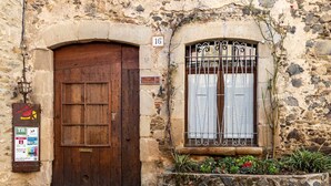 A stone building with a wooden door and a window with metal bars. There is a sign with the number 16 and another with the number 15. - Can Ventura - relaxation in nature (Sant Feliu De Pallerols)
