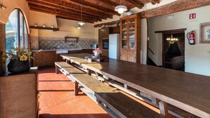 A rustic kitchen with wooden benches, a large wooden table, and a stone fireplace. - Can Ventura - relaxation in nature (Sant Feliu De Pallerols)