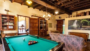 A pool table with a cue ball and a floral-patterned sofa in a room with wooden cabinets and a chandelier. - Can Ventura - relaxation in nature (Sant Feliu De Pallerols)