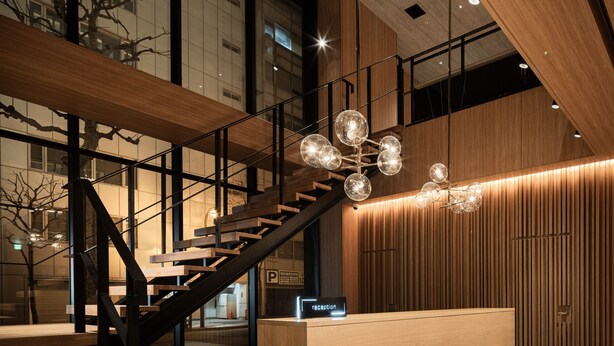 A modern reception area with a wooden reception desk, a staircase, and a unique spherical chandelier. - Bespoke Hotel Sapporo (Sapporo)
