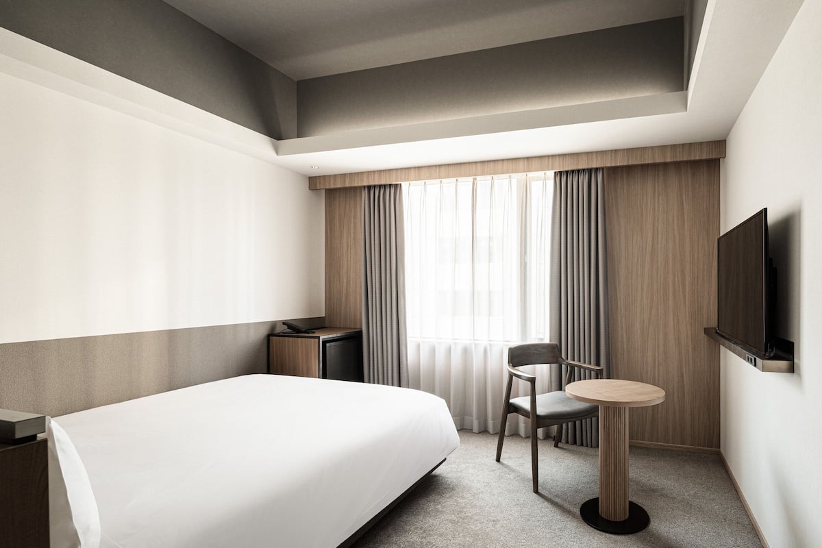 A hotel room with a large bed, a desk, a chair, a television, and a window with curtains.