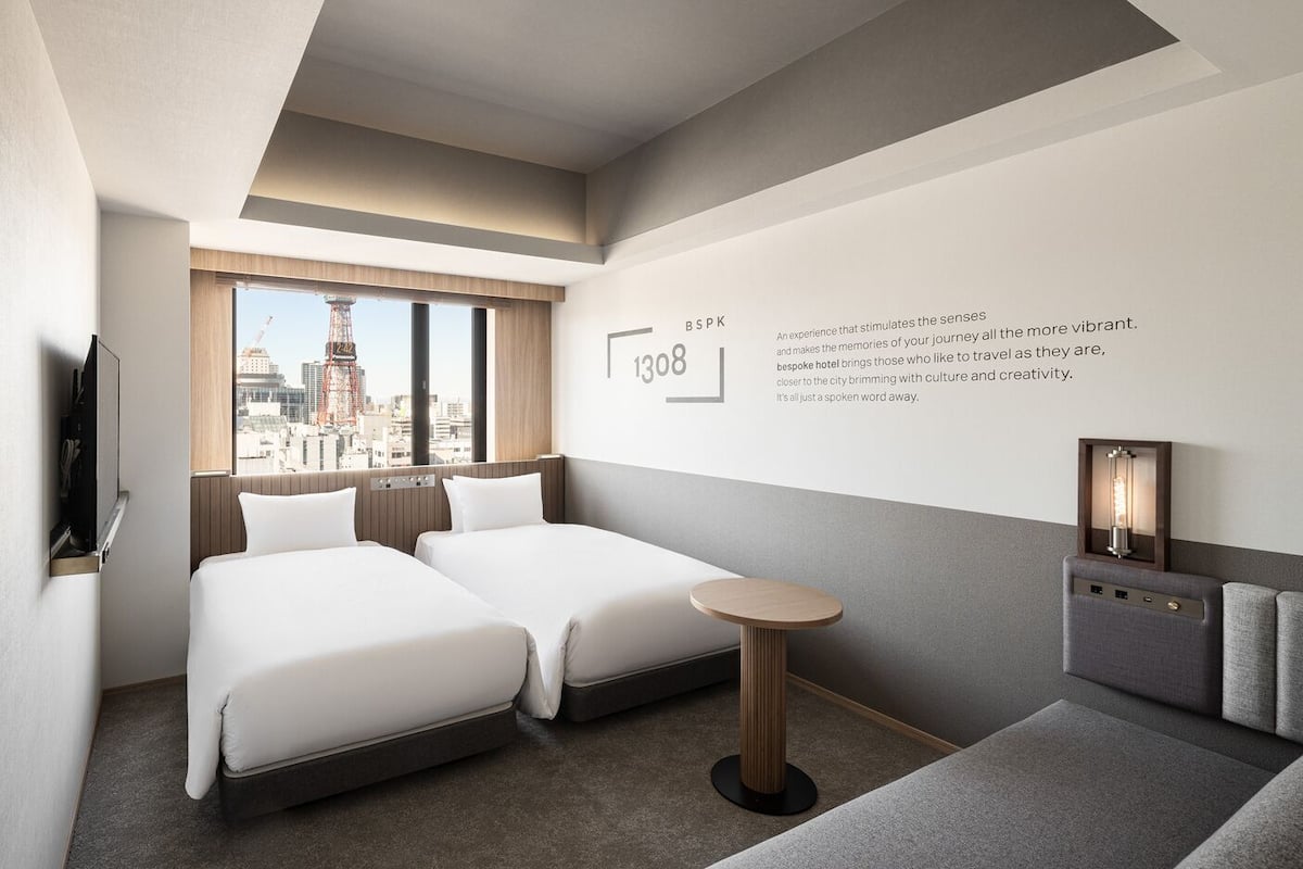 A hotel room with two beds, a small round table, a TV, and a city view.