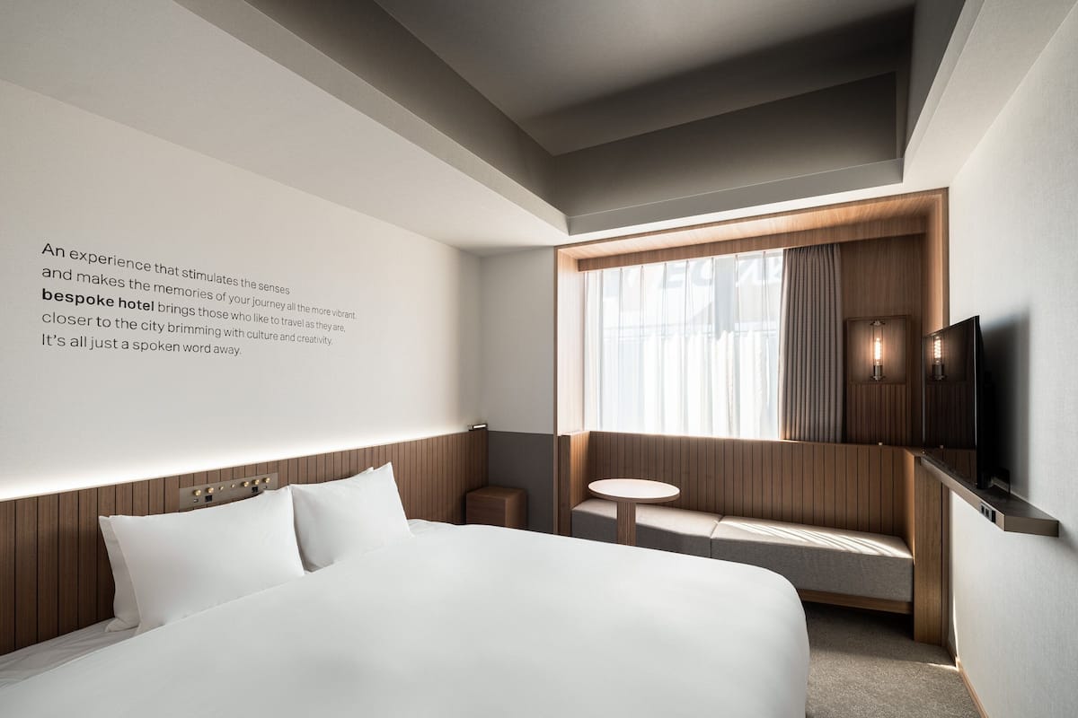 A modern hotel room with a large bed, a small seating area, a television, and a window with curtains.