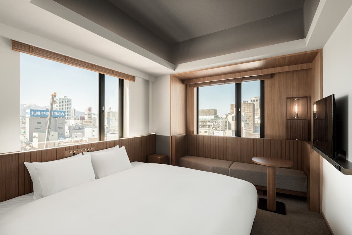 A modern hotel room with a large bed, a seating area, a TV, and a city view.