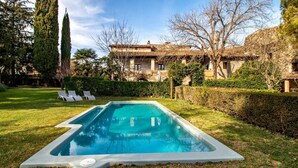 A rectangular swimming pool with a white edge, surrounded by a well-maintained lawn and a hedge.