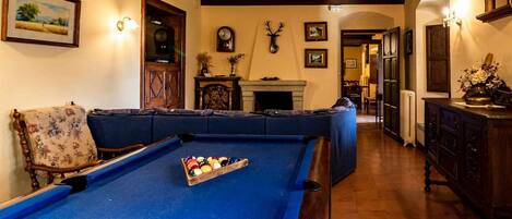 Una mesa de billar con bolas, un sofá, una chimenea y un reloj en la pared.