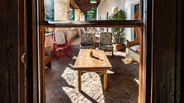 An outdoor patio area with a wooden table and chairs, a red chair, and potted plants.