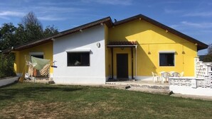 A two-story house with a yellow and white exterior, a front porch with chairs, and a small garden area. - Inviting 4-Bed Villa in Dolishte (Varna)