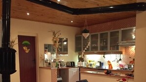 A cozy living room with a fireplace, a dining area, and a kitchen with wooden cabinets and a hanging light fixture. - Inviting 4-Bed Villa in Dolishte (Varna)
