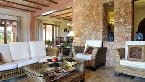 A cozy living area with wicker furniture, a glass coffee table, and a stone wall. - Finca Mimosa - haven of peace with amazing views (Cala D'or)