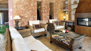 A cozy lounge area with wicker furniture, a glass coffee table, and a stone wall backdrop. - Finca Mimosa - haven of peace with amazing views (Cala D'or)