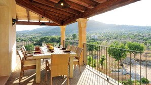 A covered outdoor dining area with a table set for four, surrounded by wicker chairs, overlooking a scenic landscape with mountains and greenery. - Finca Mimosa - haven of peace with amazing views (Cala D'or)