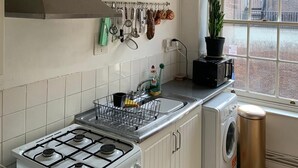 A compact kitchen with a gas stove, a built-in oven, a microwave, a sink, and a window with a view of the city. - Charming 3-Bed Apartment in London (London)