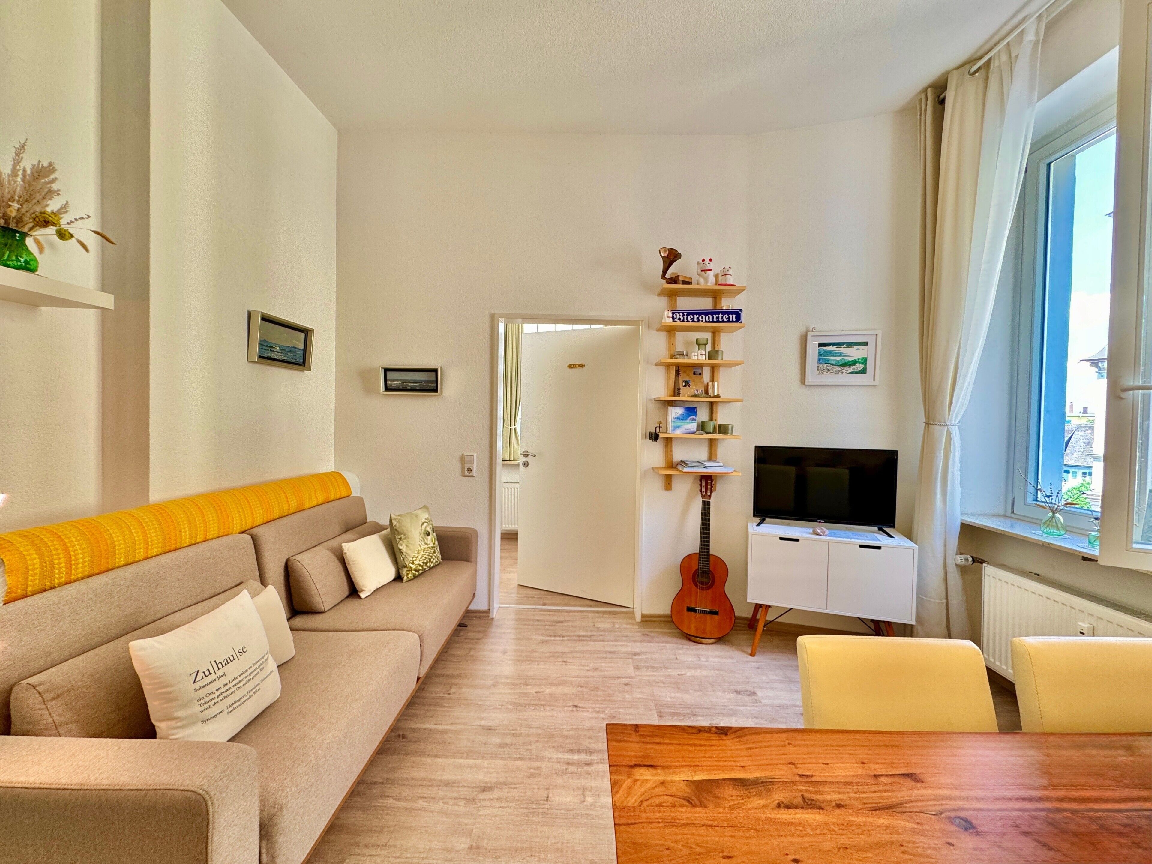 Una sala de estar con un sofá, una mesa de centro de madera, un televisor, una guitarra y una estantería.