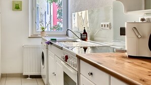 A kitchen with white cabinets, a wooden countertop, a window with a view of buildings, a radiator, and a washing machine.