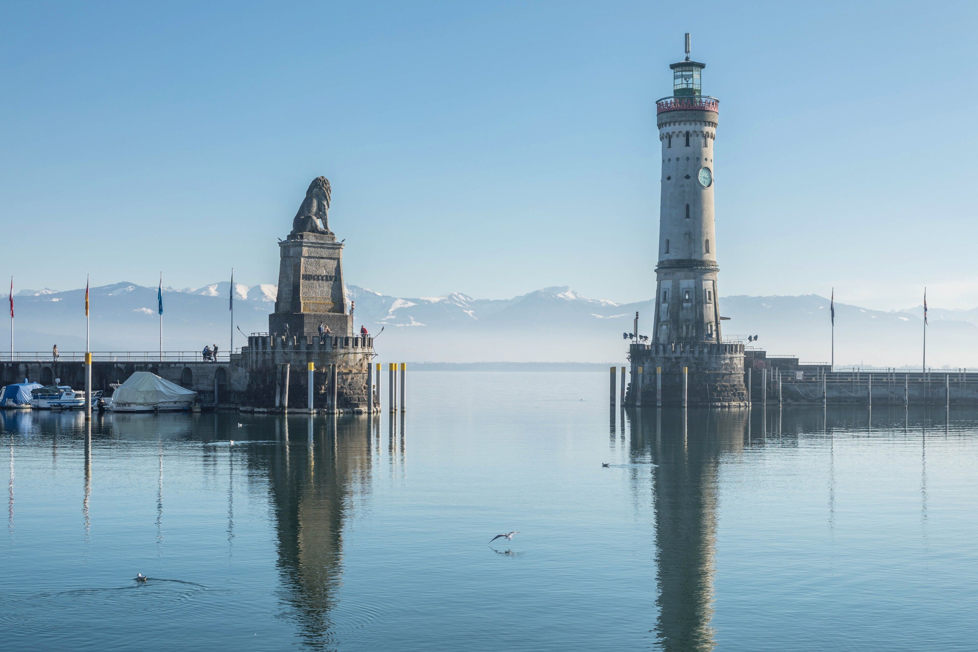 Un puerto tranquilo con un faro y una estatua, rodeado de montañas.