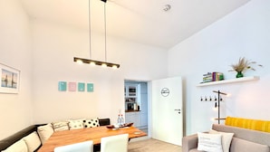 A modern living space with a dining area, sofa, and a kitchen in the background.