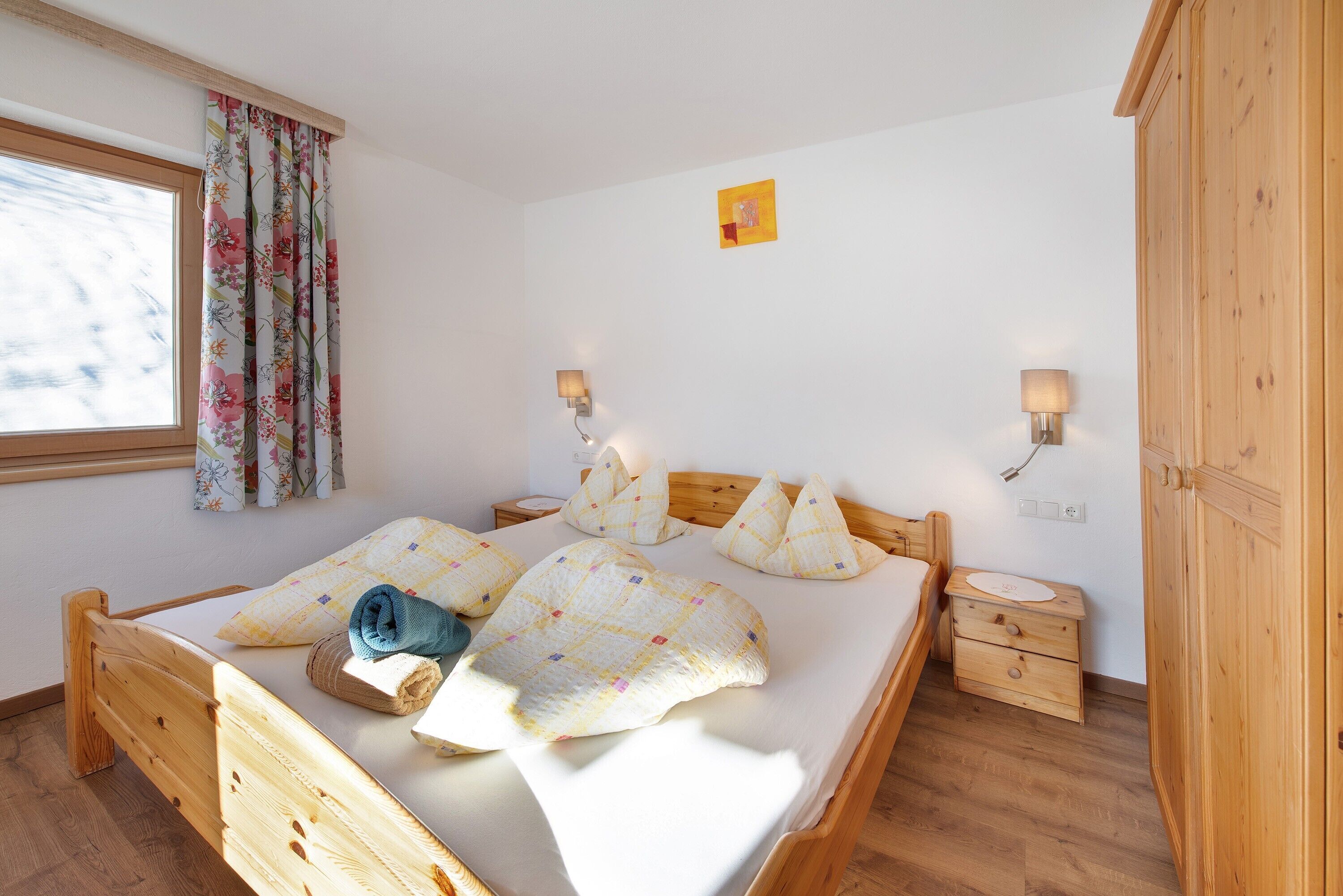 Ein hölzernes Bett mit Kissen, ein Nachttisch, eine Lampe und ein Fenster mit Vorhängen.