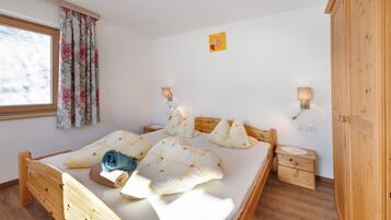 Ein hölzernes Bett mit Kissen, ein Nachttisch, eine Lampe und ein Fenster mit Vorhängen.