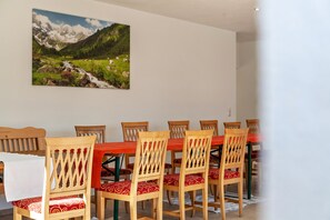 Un coin repas avec une table et des chaises en bois, un tableau représentant un paysage montagneux et un mur blanc.