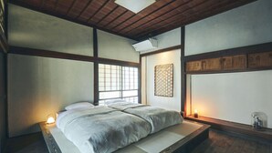 A traditional Japanese-style room with tatami flooring, a low platform bed, shoji screens, and a wooden ceiling. - Kominka yado LOOF Kyo no ie (Hokuto)