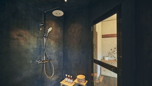 A small, dark bathroom with a shower, a wooden stool, and a small table with toiletries. - Kominka yado LOOF Kyo no ie (Hokuto)