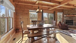 L’intérieur d’un chalet en bois comprend une table à manger, des chaises, une cheminée et de grandes fenêtres.