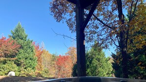 Un bain à remous entouré d’arbres aux feuilles d’automne, une structure en bois et un ciel bleu dégagé.