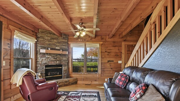 L’intérieur d’une cabane en rondins, avec une cheminée en pierre, un canapé en cuir et un ventilateur de plafond.