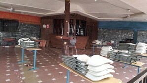 Une pièce spacieuse avec un plafond haut, plusieurs ventilateurs de plafond et un pilier central. Des tables sont disposées et présentent divers objets, notamment des chaises pliantes et des objets empilés.