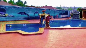Une piscine ornée d’une fresque représentant des dauphins, une fontaine et un petit bâtiment doté d’un toit en tuiles.