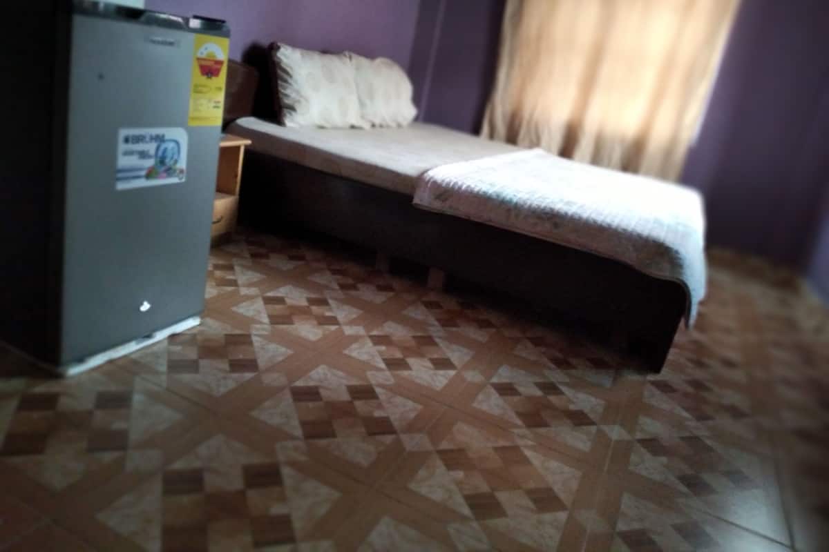 A small room with a bed, a nightstand, and a refrigerator.
